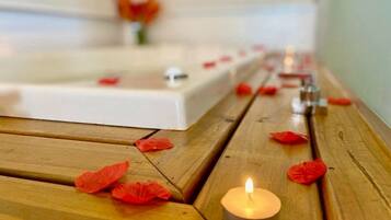 A wooden bench with a lit candle and scattered rose petals.