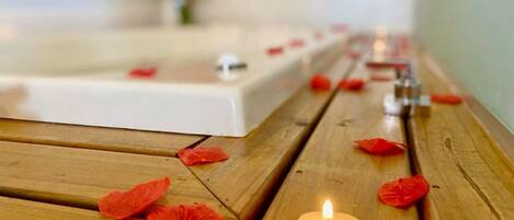 A wooden bench with a lit candle and scattered rose petals.