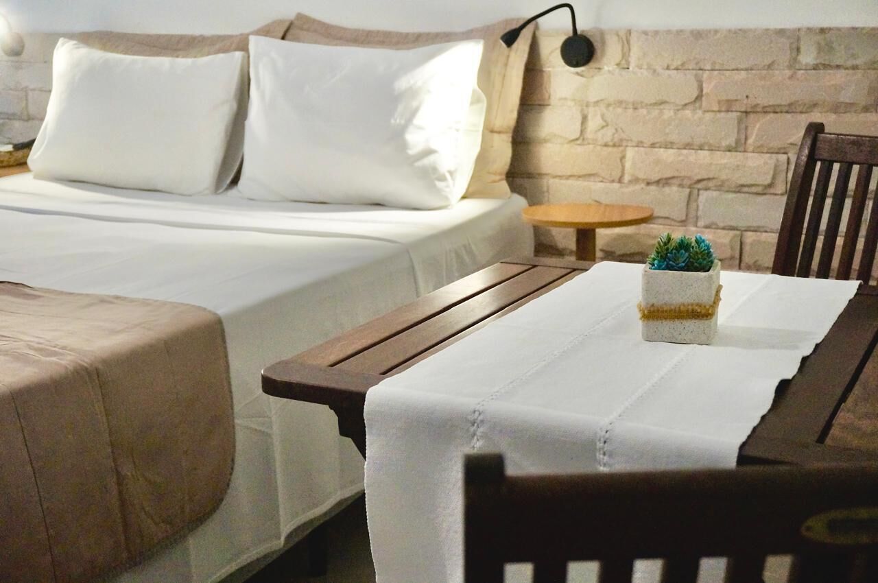 A neatly made bed with white linens and pillows, a small wooden table with a white tablecloth, and a potted succulent plant.