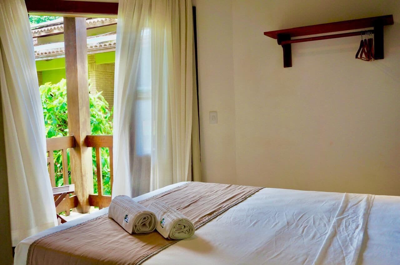 Una habitació d'hotel amb un llit, una finestra amb cortines i una barana de balcó de fusta.