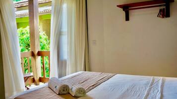 Una habitació d'hotel amb un llit, una finestra amb cortines i una barana de balcó de fusta.
