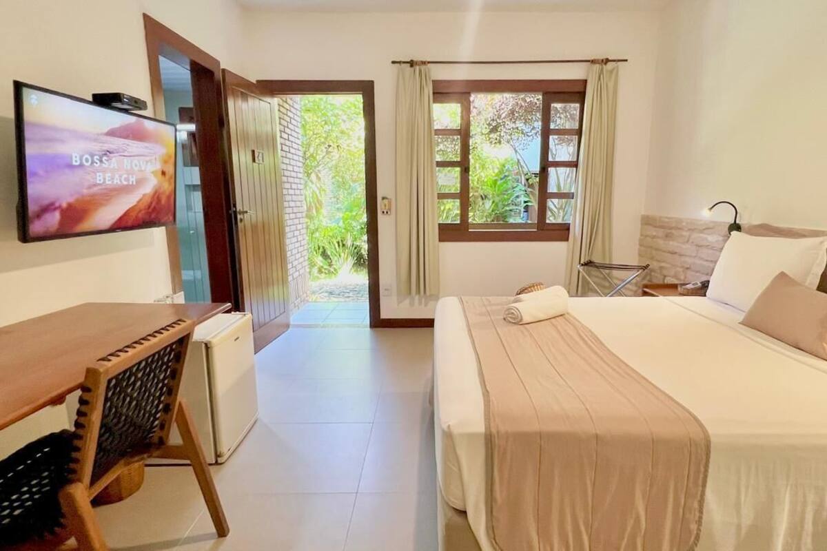 A hotel room with a bed, a desk, a TV, and a view of the garden.