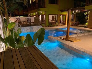 Een zwembadgedeelte met een houten terras, een bubbelbad en een overdekte zithoek.