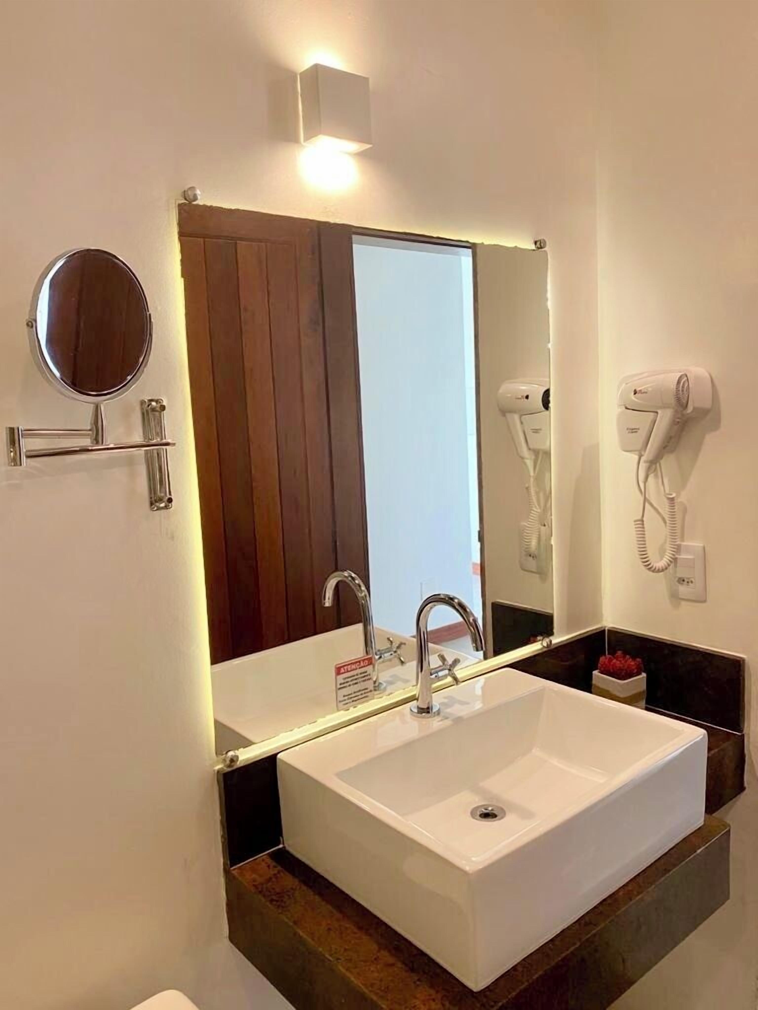 A modern bathroom with a white sink, a large mirror, a hairdryer, and a towel rack.