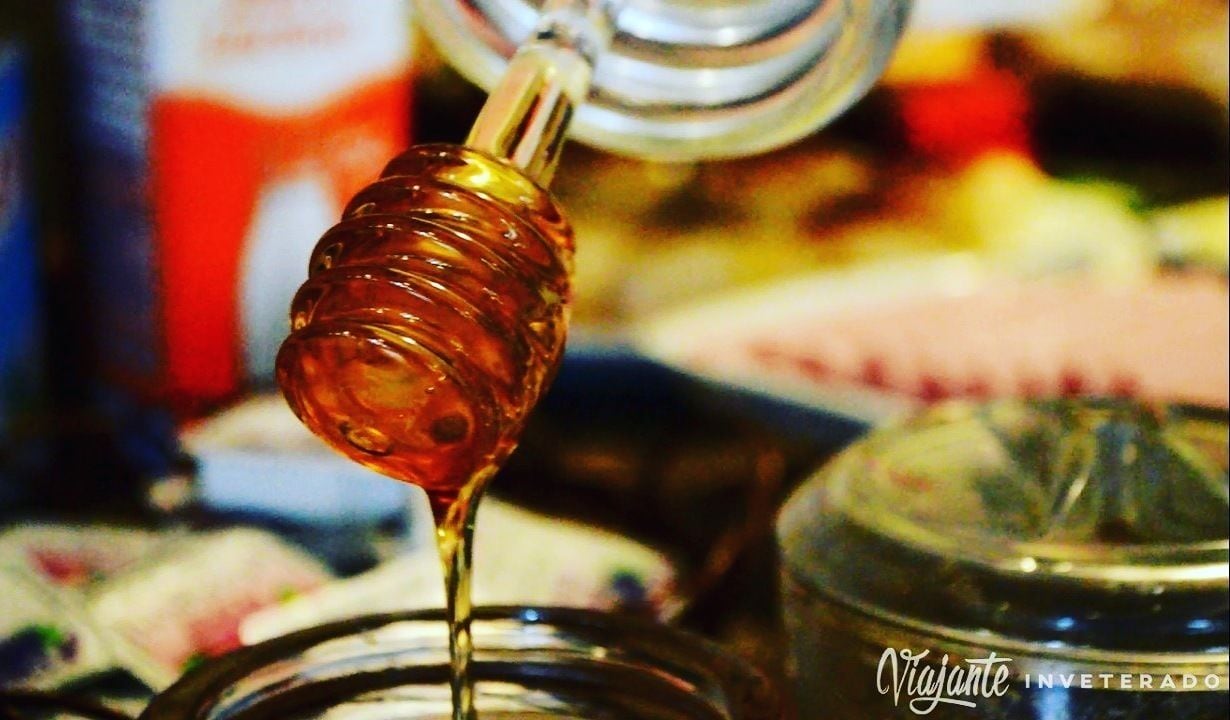 A close-up of a honey dipper dripping honey into a jar.