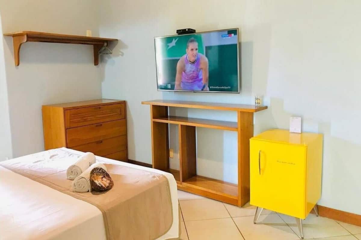 A hotel room with a bed, a wooden dresser, a yellow cabinet, and a television mounted on the wall.