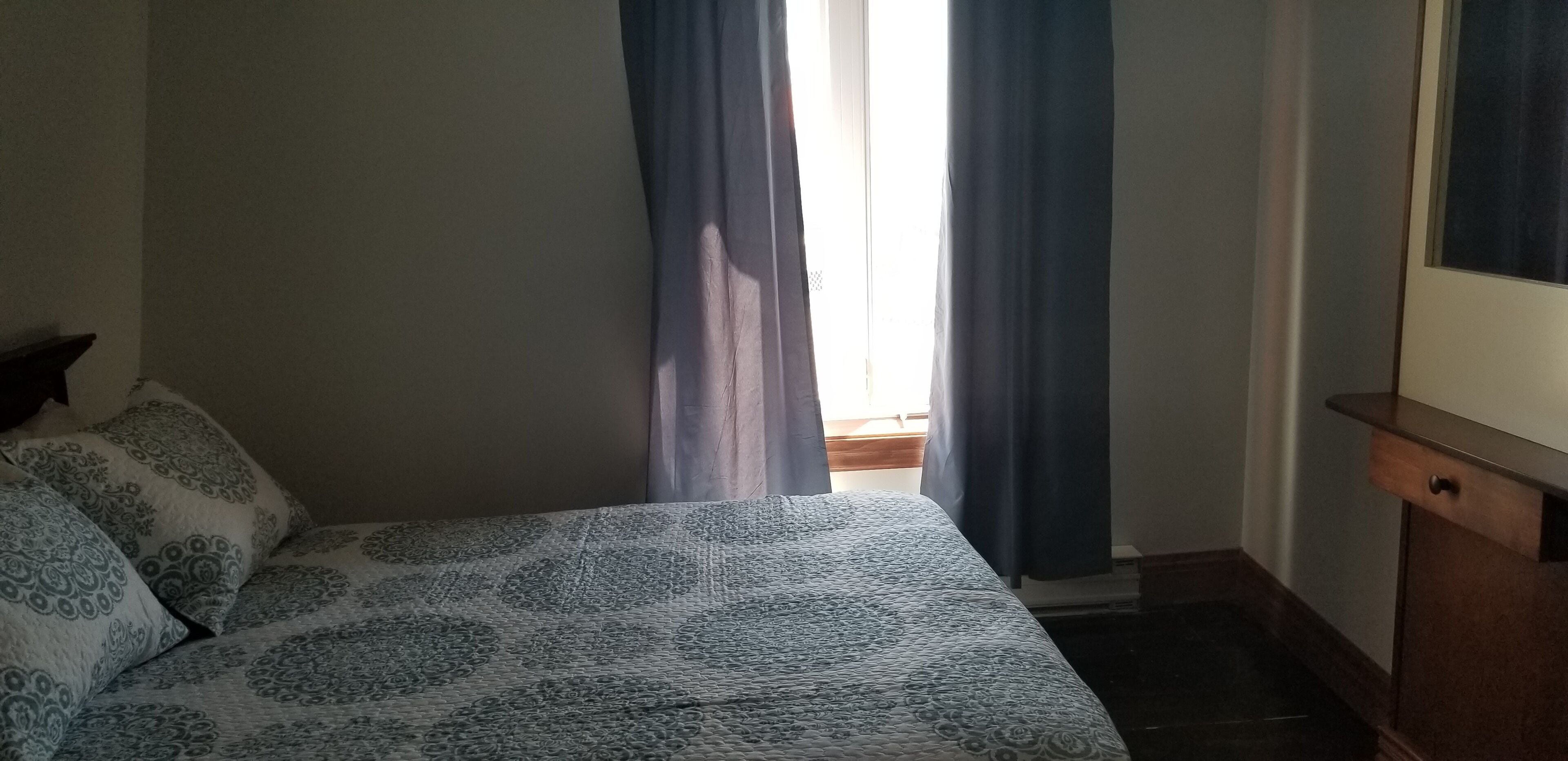 Un dormitorio con cama, mesita de noche, cómoda y ventana con cortinas.