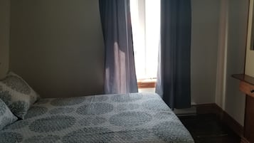 Un dormitorio con cama, mesita de noche, cómoda y ventana con cortinas.