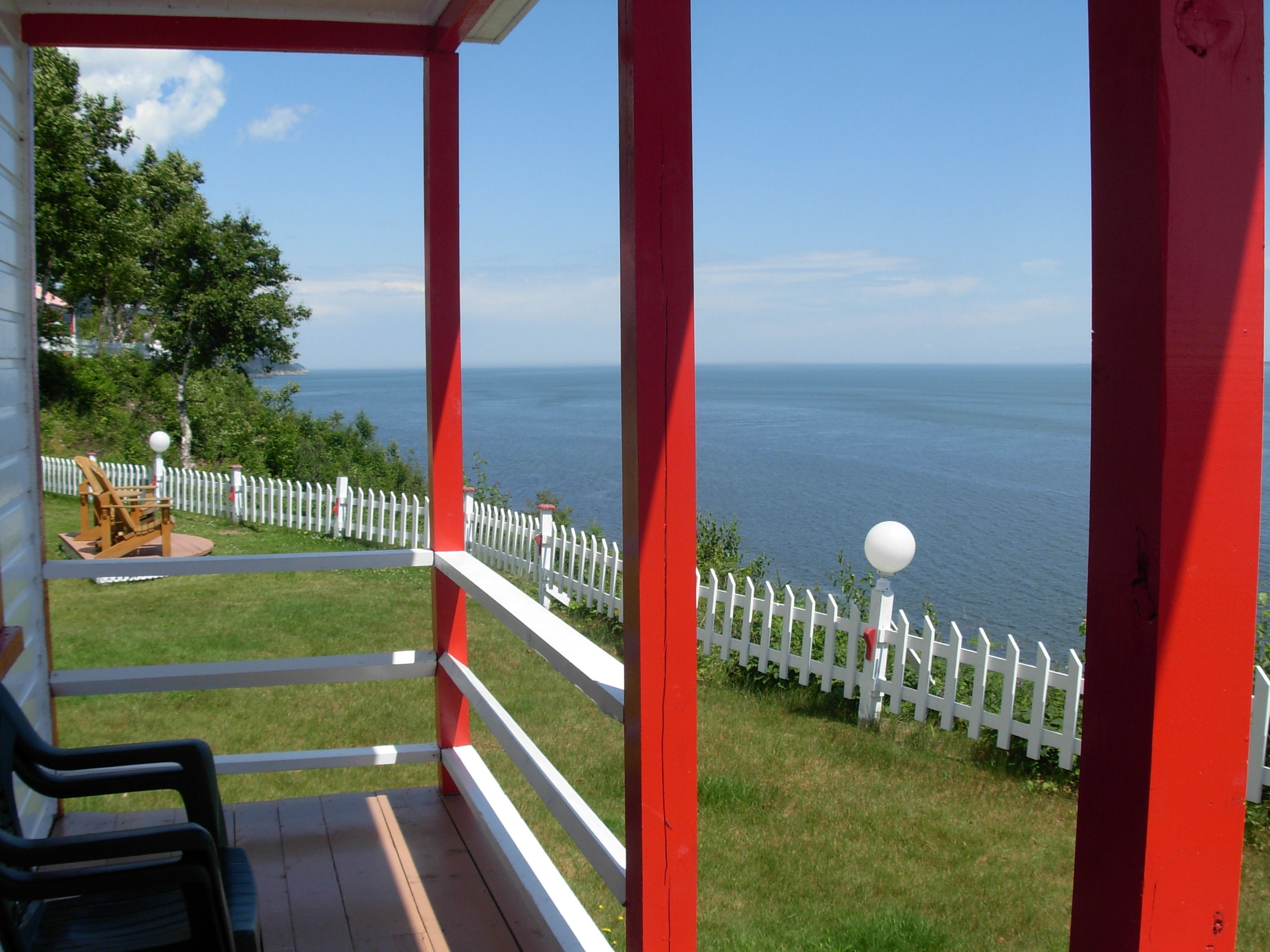 A balcony with a white picket fence, a wooden deck, and a view of the sea.