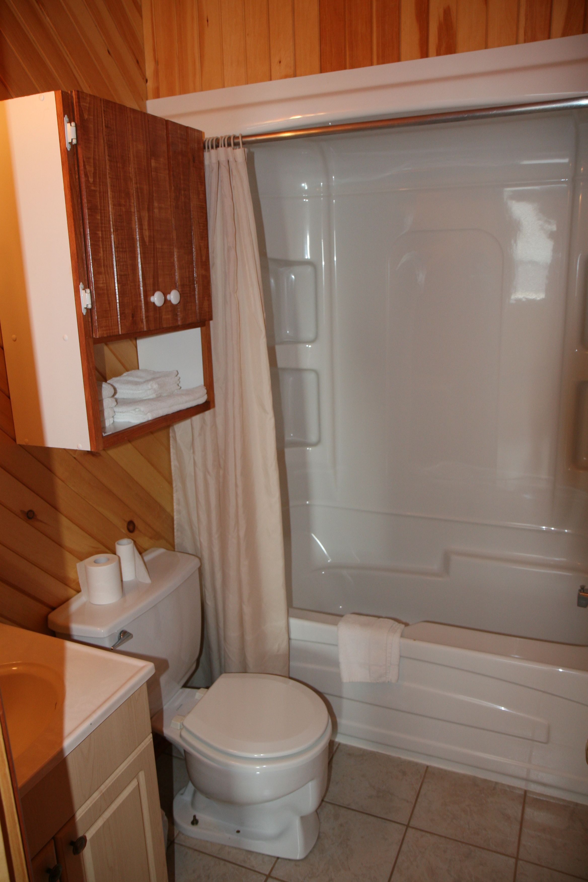 Un baño con inodoro, ducha y un mueble de madera sobre el inodoro.
