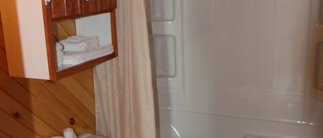 Un baño con inodoro, ducha y un mueble de madera sobre el inodoro.