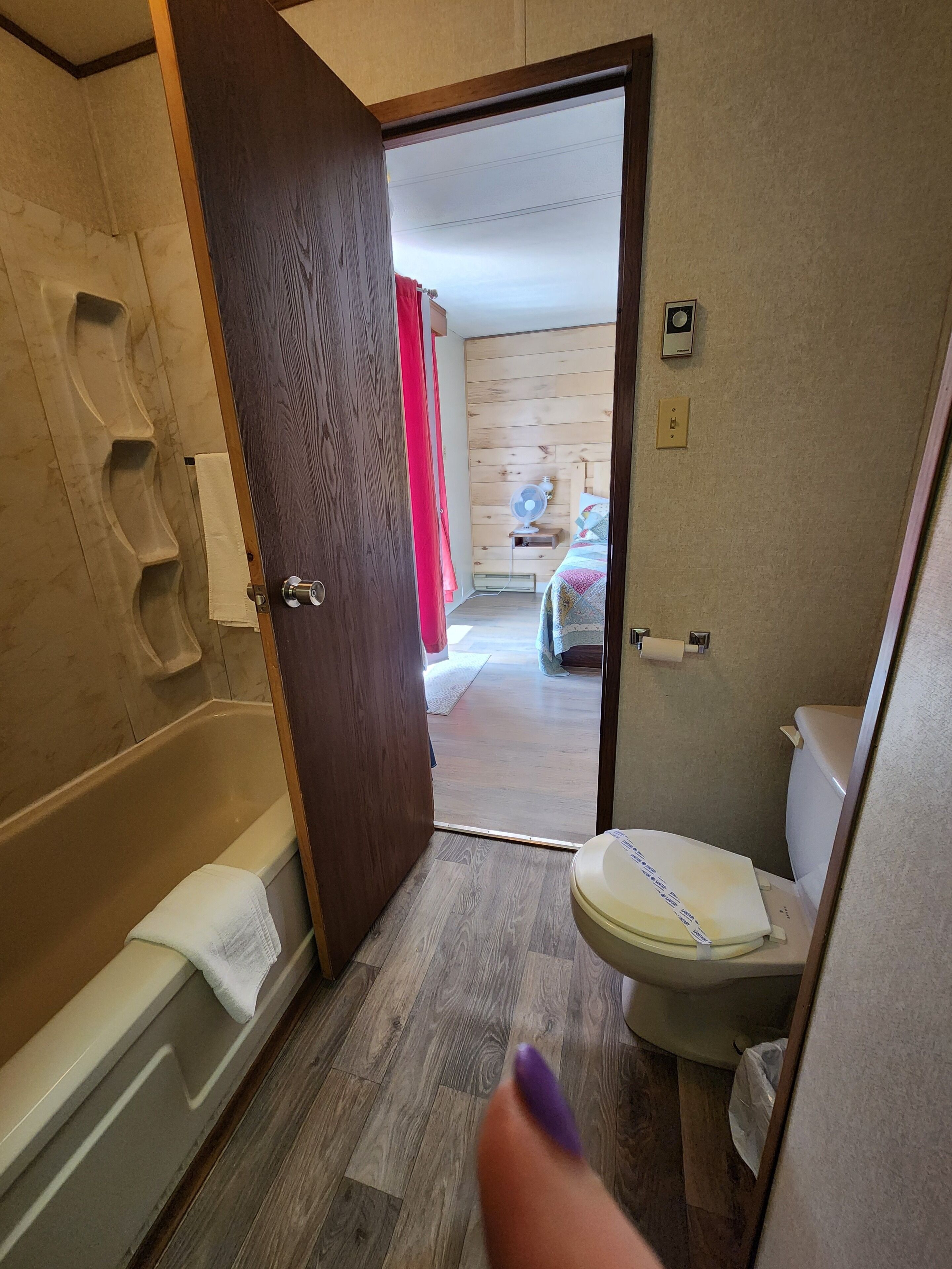 A bathroom with a bathtub, toilet, and wooden panel walls.