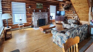 Ein Blockhaus-Interieur mit Kamin, Holzböden, einer Couch und einem Fernseher.