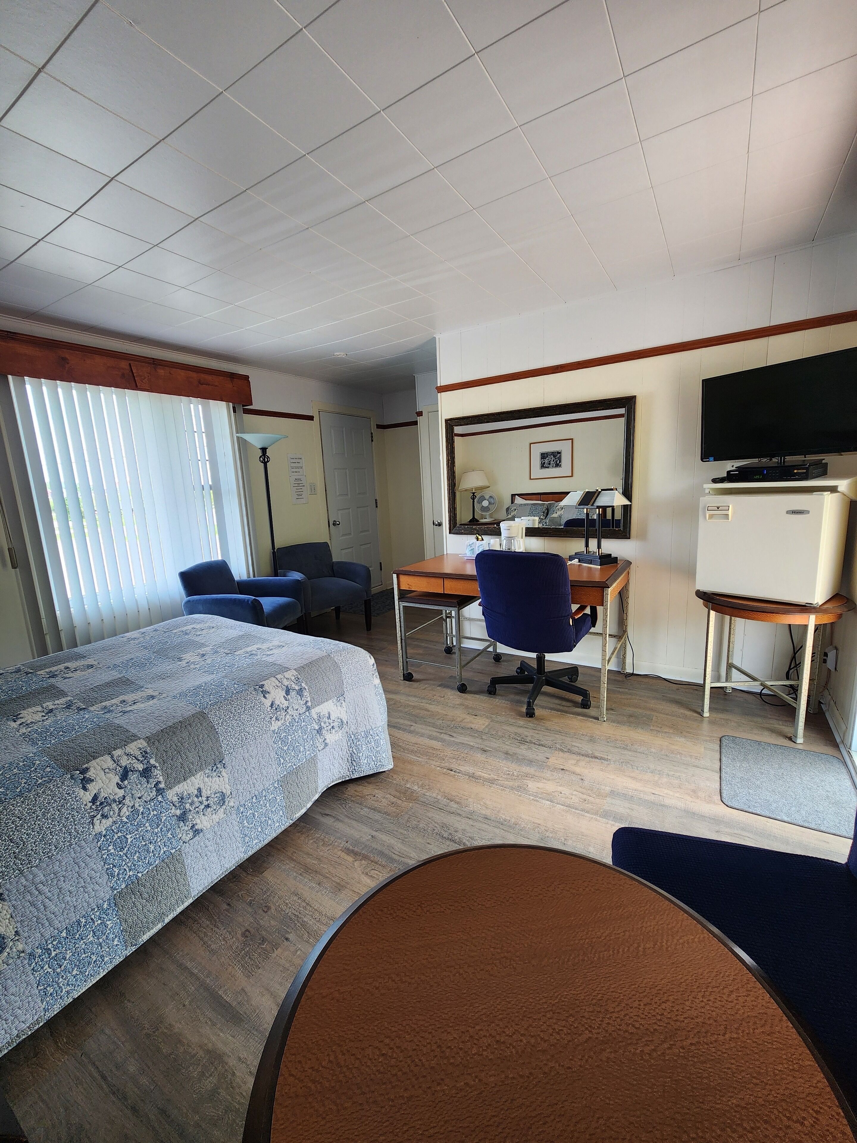 Una habitación de hotel con cama, escritorio, silla, televisor y refrigerador.