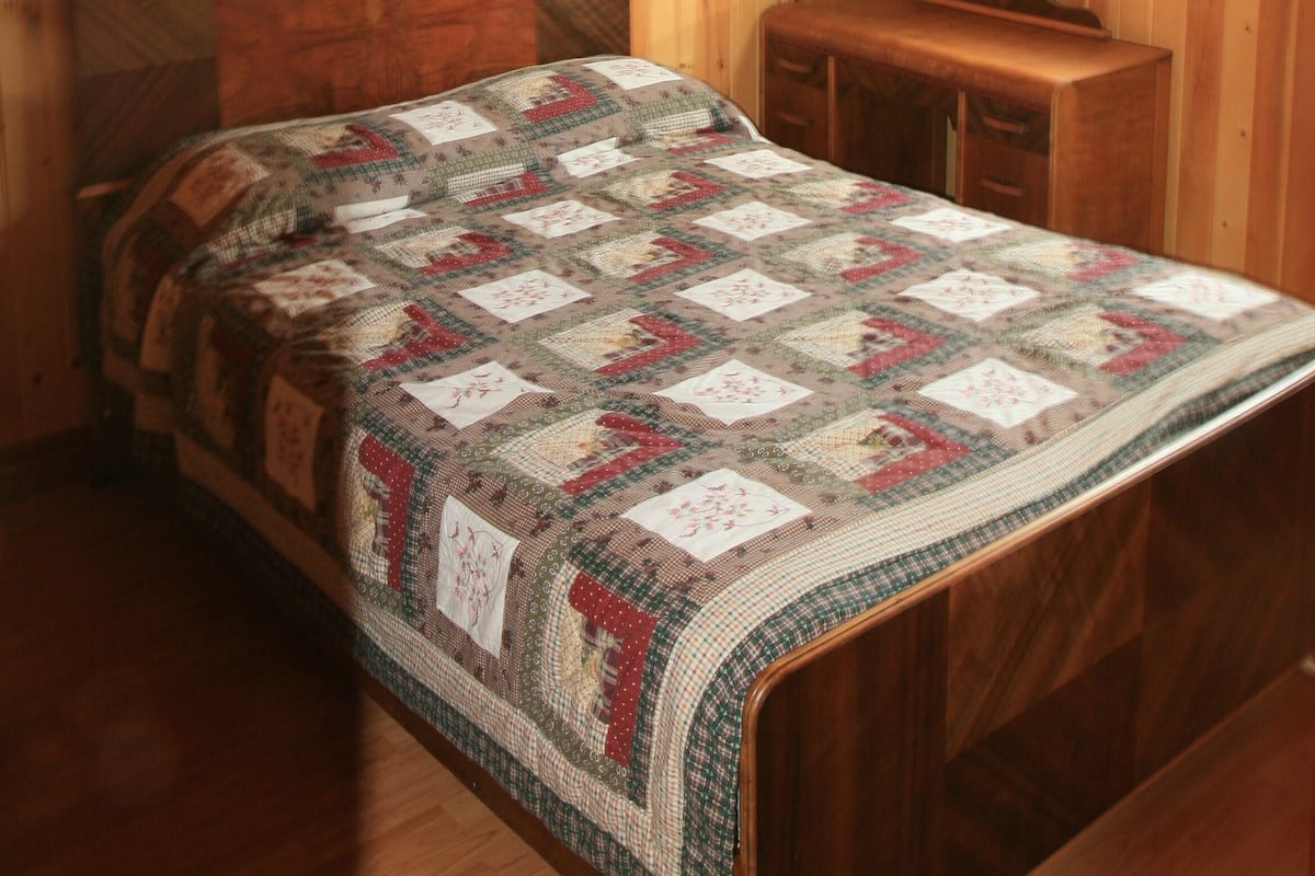 Un dormitorio con techo inclinado de madera, una cama con colcha, un aparador de madera y un espejo.