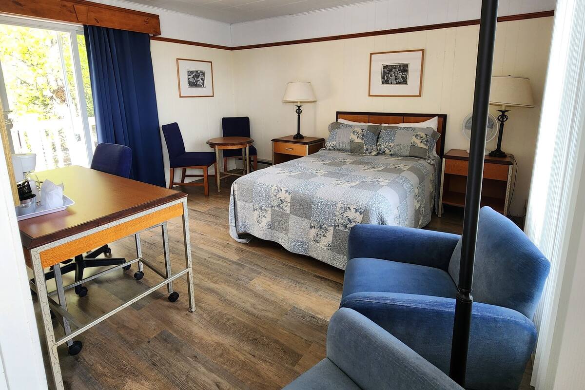 Habitación de hotel con cama, escritorio, silla, lámpara de pie y ventana con cortinas.
