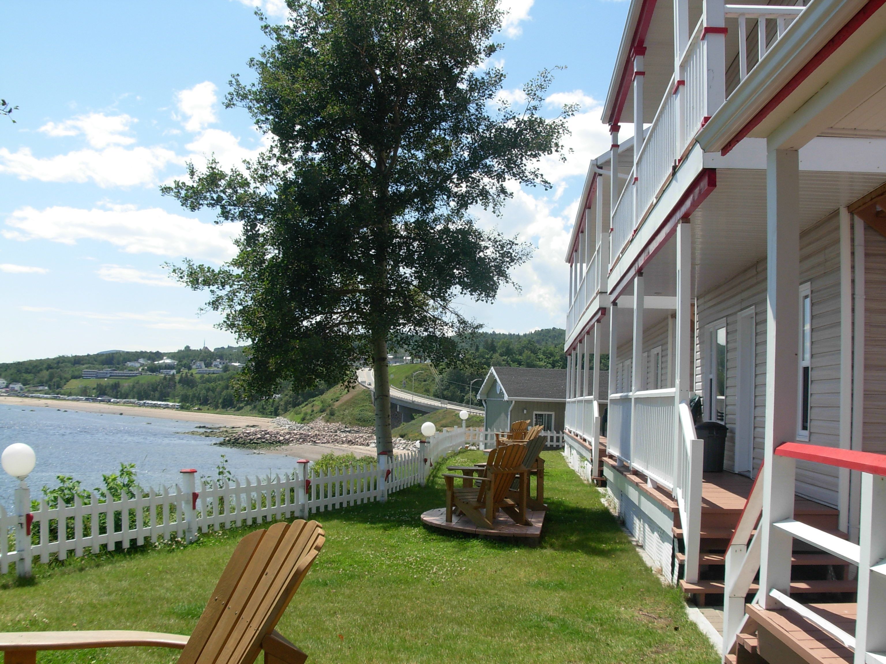 A coastal hotel with a balcony overlooking the beach, a white picket fence, and a wooden deck with chairs.