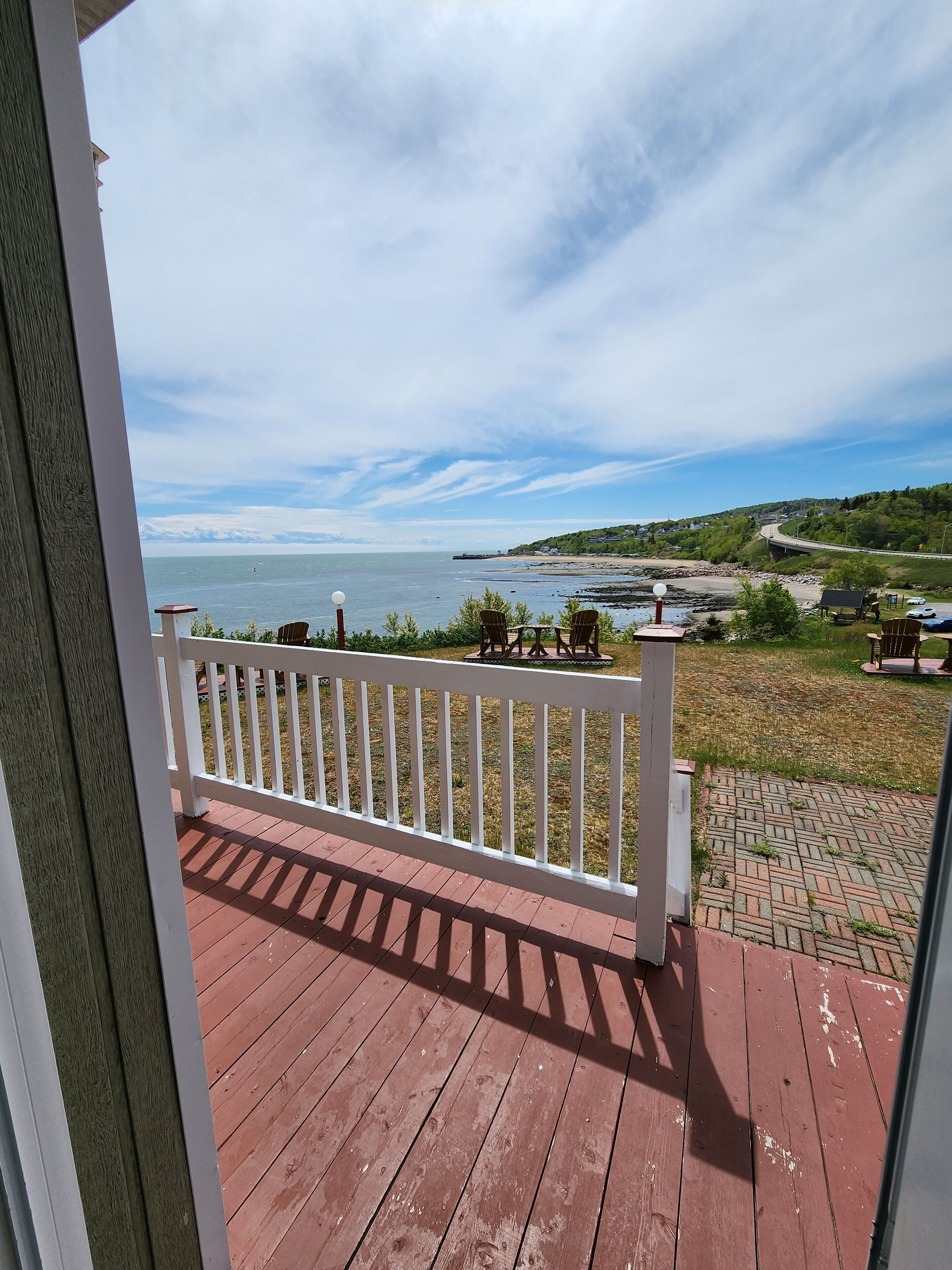 A wooden deck with a white railing, overlooking a beach and a road with vehicles.
