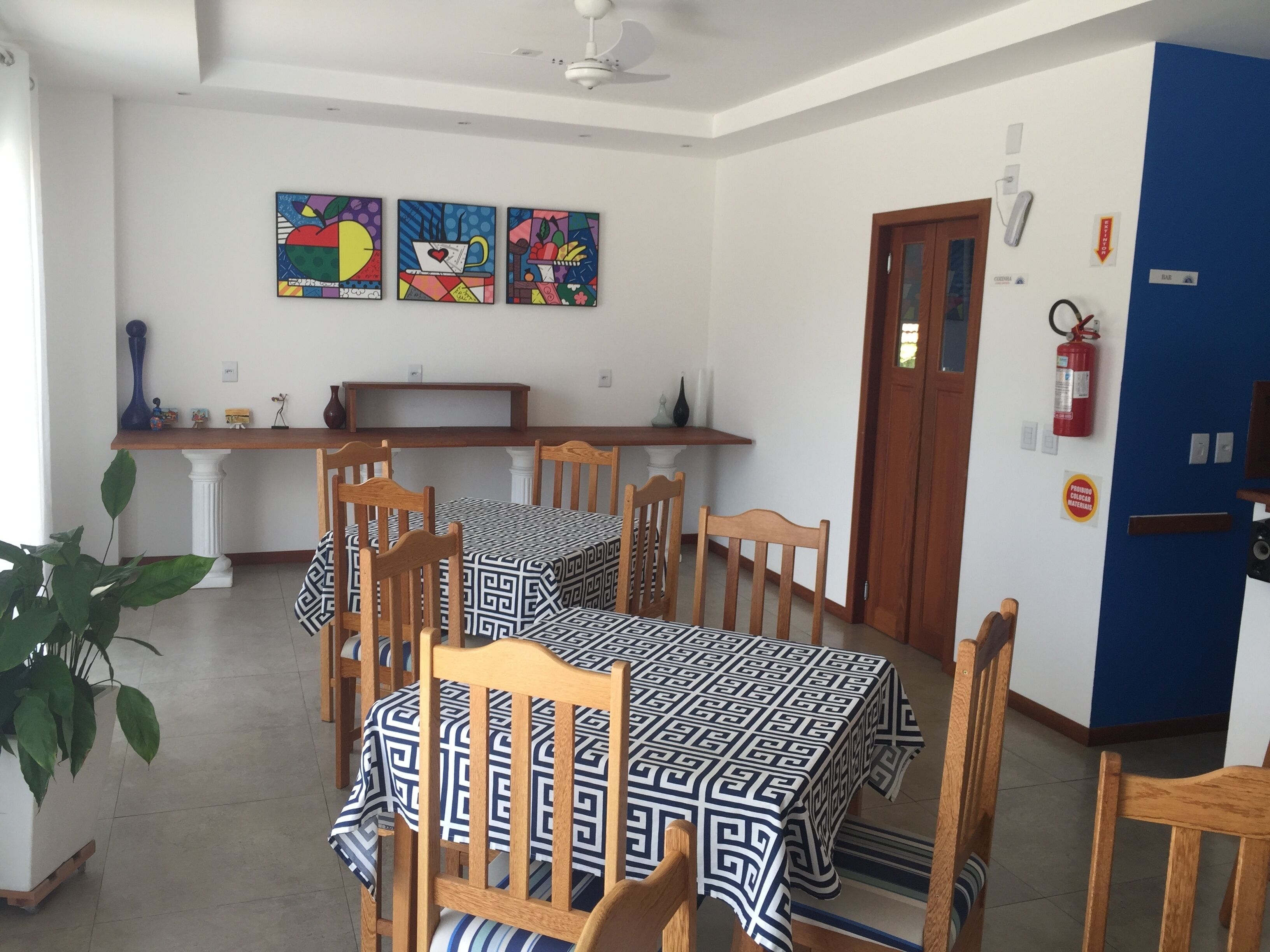 A dining area with a table set for four, surrounded by wooden chairs. There are three paintings on the wall above the table.