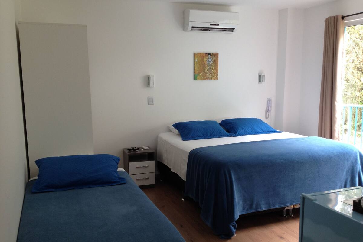 A bedroom with two beds, a nightstand, an air conditioner, and a window with curtains.