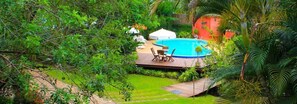 A backyard with a swimming pool, surrounded by lush greenery and a wooden deck. - Pousada Atlântica (Itacaré)