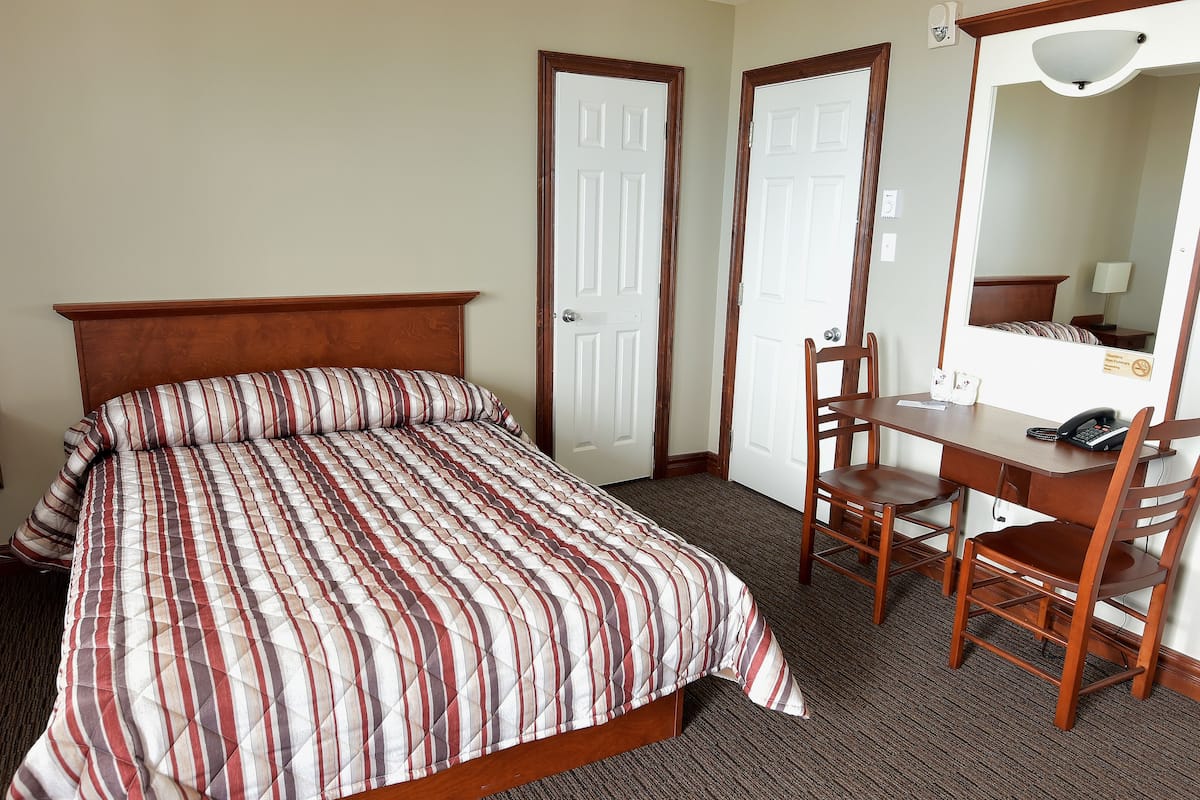 A hotel room with a bed, a desk, two chairs, a mirror, and two doors.