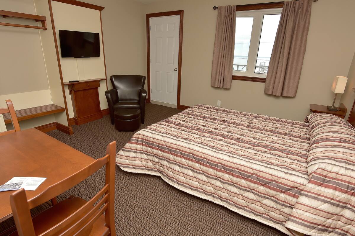 A hotel room with a bed, a desk, a chair, a television, and a window with curtains.