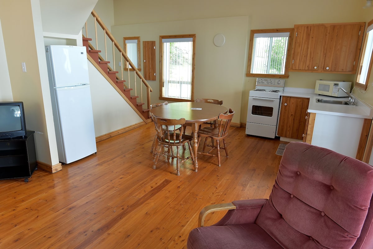 A kitchen with wooden cabinets, a dining table with chairs, a refrigerator, a microwave, and a stove.