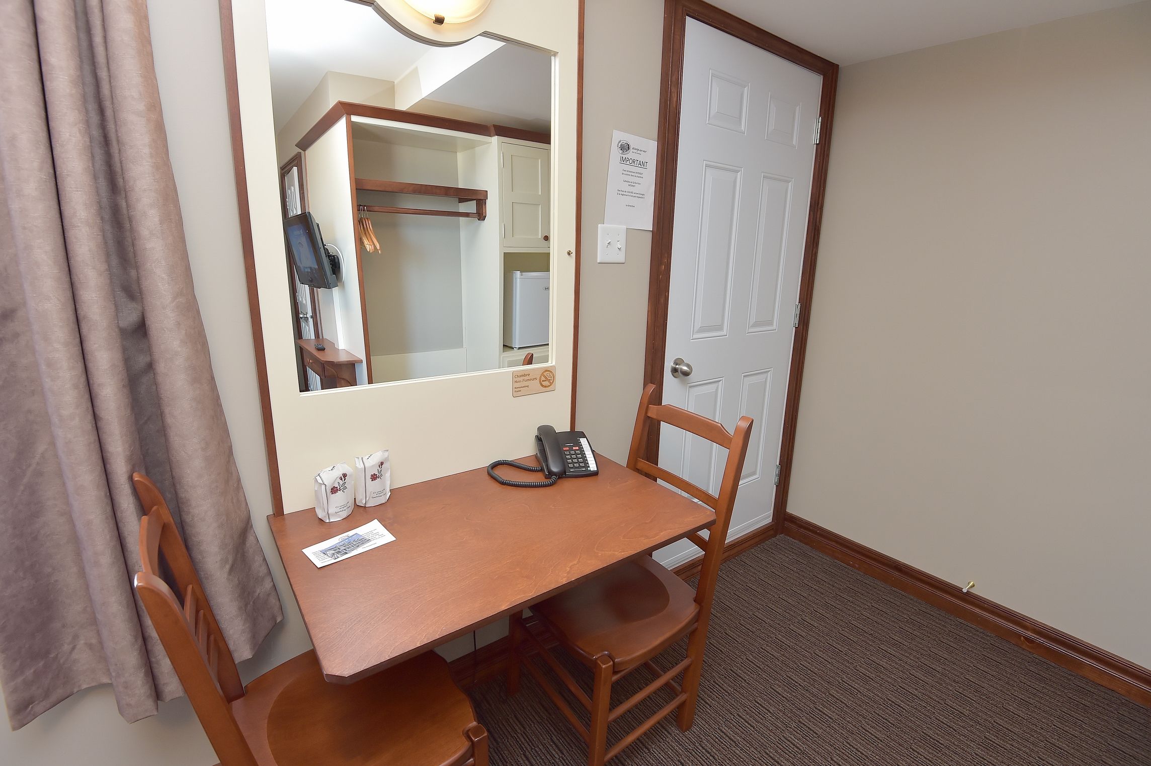 A hotel room with a wooden desk, a telephone, and a mirror.