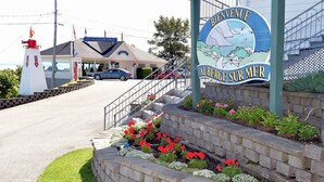 Schild für Auberge Sur Mer mit Leuchtturm und Restaurant im Hintergrund.