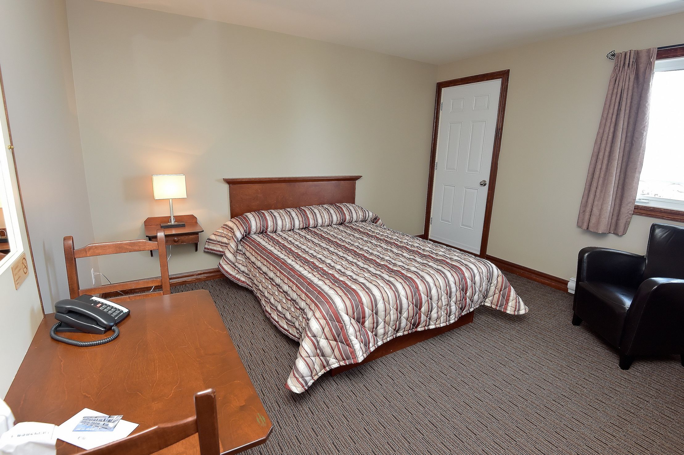 Een hotelkamer met een bed, een bureau met telefoon, een stoel en een lamp.