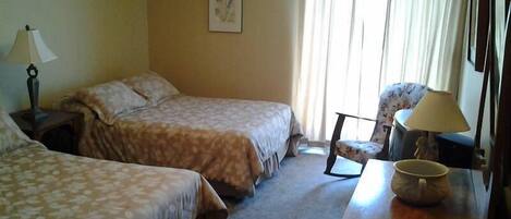 Habitación de hotel con dos camas, una silla, un escritorio con lámpara y una ventana con cortinas.