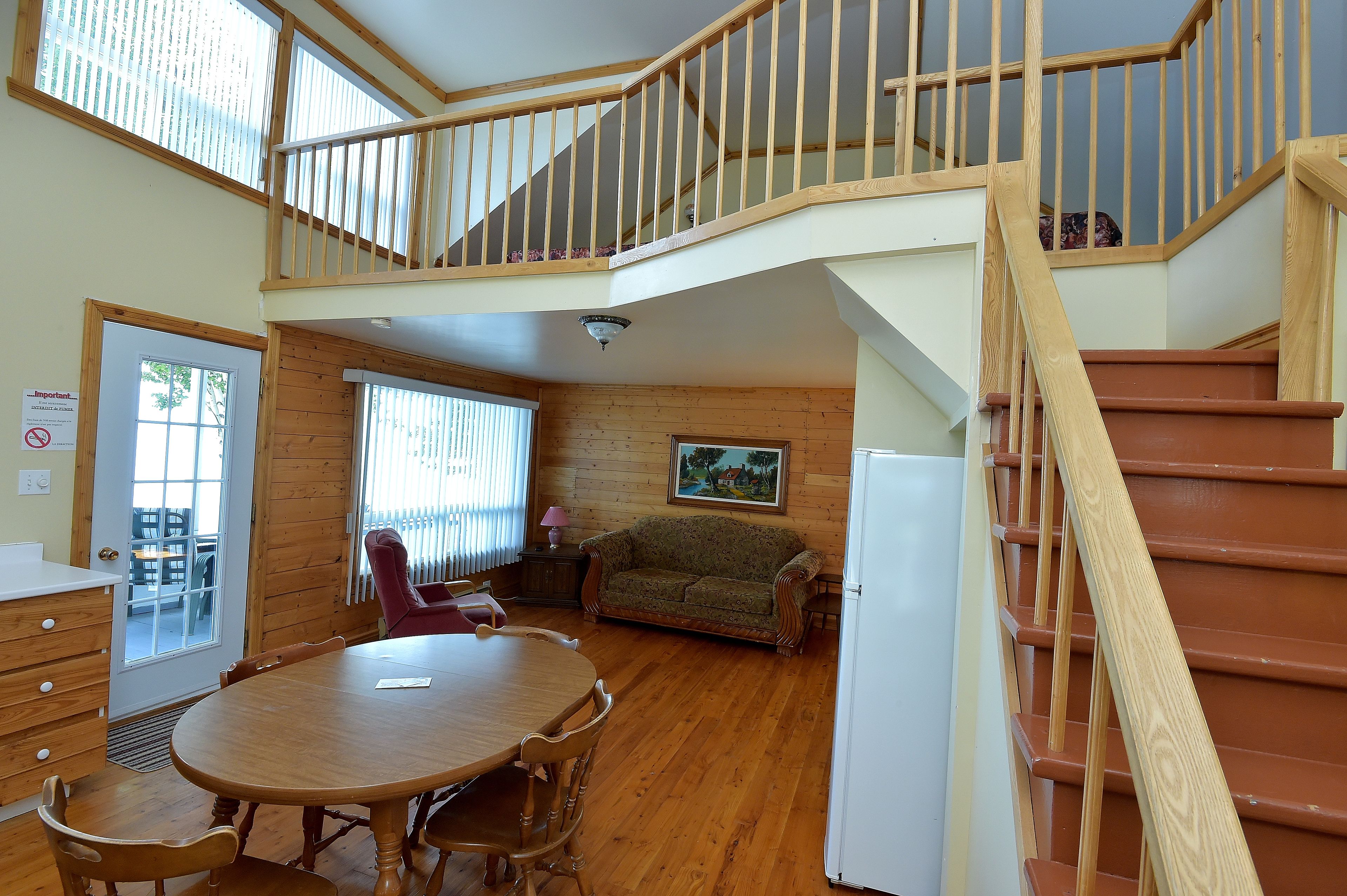 A spacious room with a wooden staircase, a dining table with chairs, a sofa, and a refrigerator.