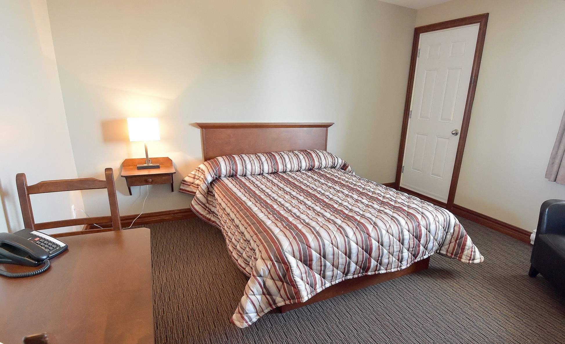 Une chambre d’hôtel avec un lit, un bureau avec un téléphone, une table de chevet avec une lampe et une porte.