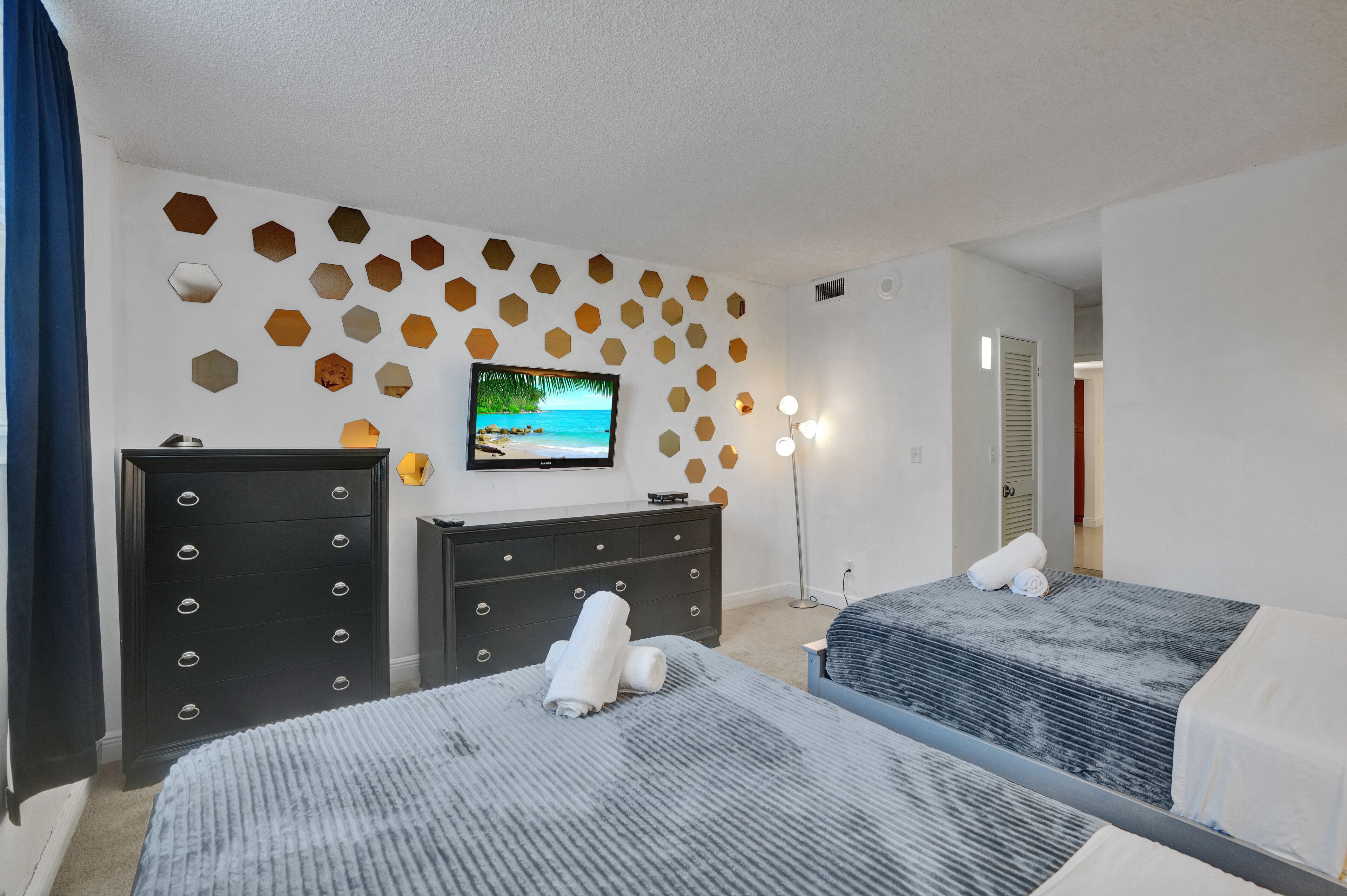 Ein Hotelzimmer mit zwei Betten, einem Schminktisch, einem Fernseher und einer Wand mit sechseckartigen Verzierungen.