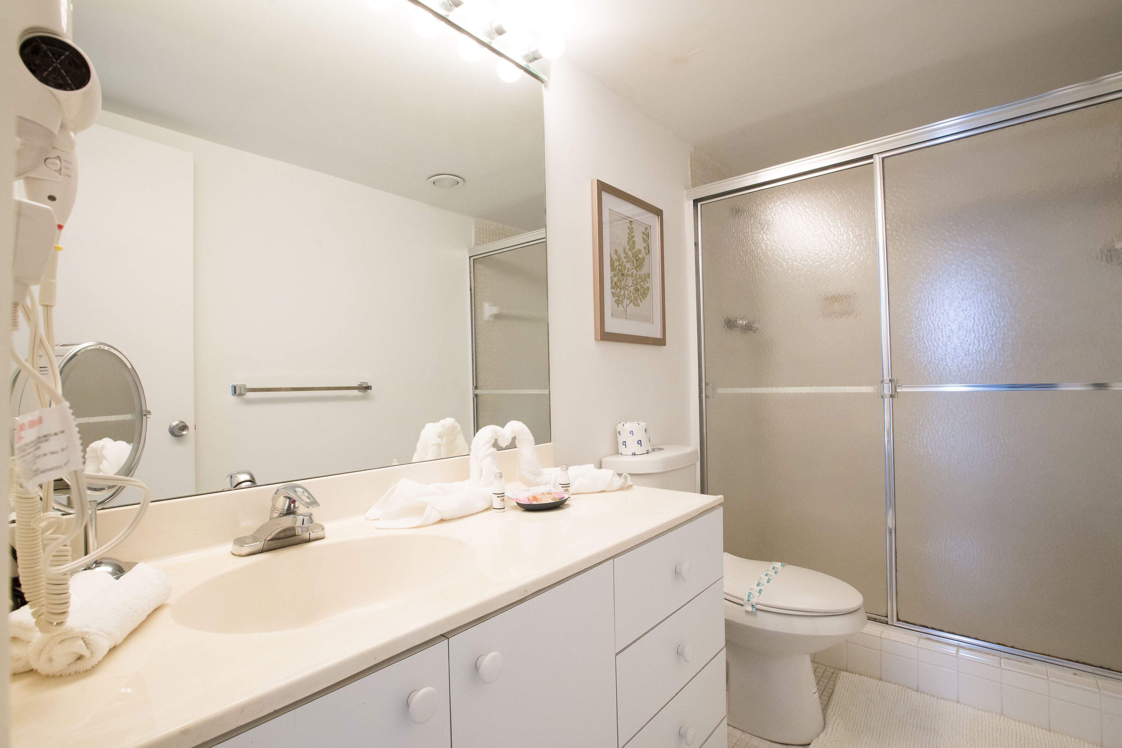 A bathroom with a large mirror, a sink, a toilet, and a shower enclosure.