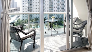 A balcony with wicker furniture, a small table with a flower, and a view of a cityscape and parking lot. - Ocean Reserve Luxury Condos Across from Sunny Isles Beach (Sunny Isles Beach)