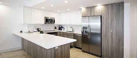 A modern kitchen with white cabinetry, a central island, stainless steel appliances, and a wooden accent wall.