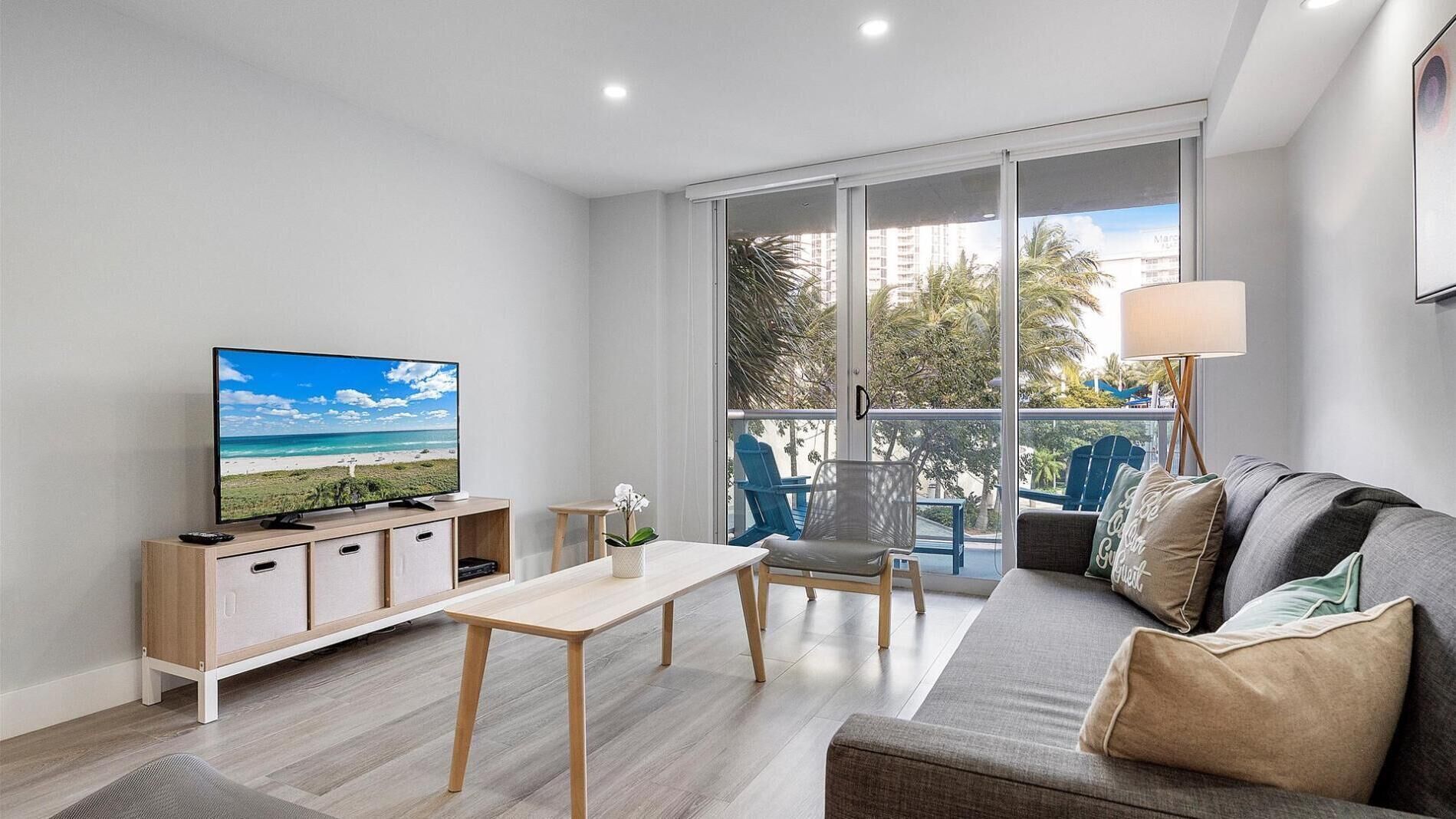 A modern living room with a television, sofa, and balcony with chairs.