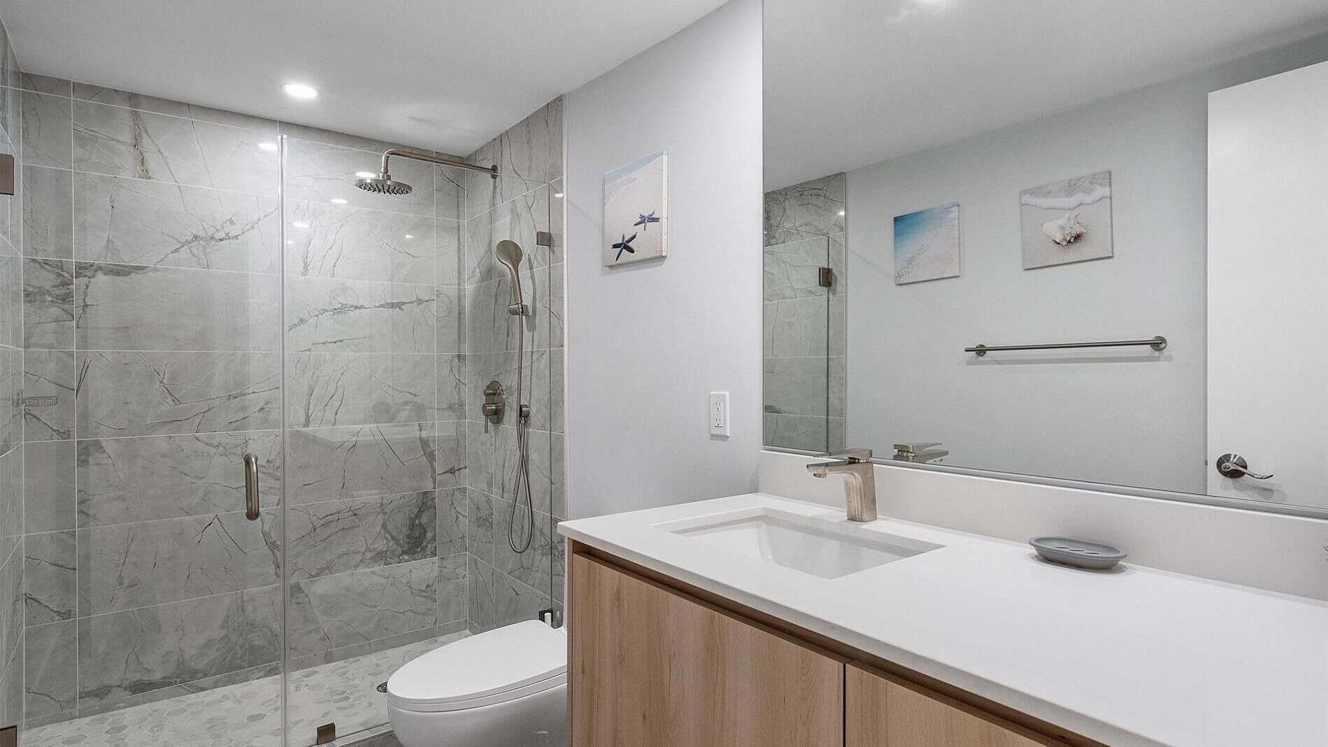 A modern bathroom with a glass-enclosed shower, a white sink, and a large mirror.