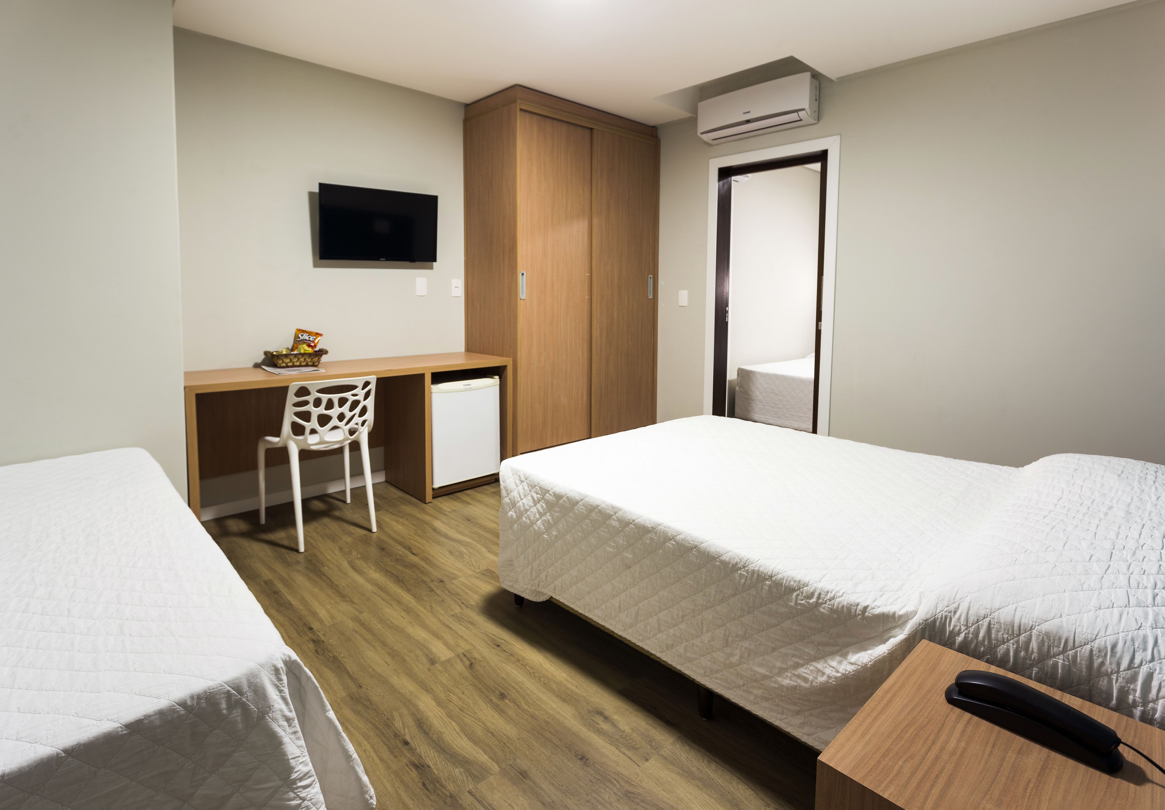 A hotel room with two beds, a desk, a chair, a television, and an air conditioning unit.