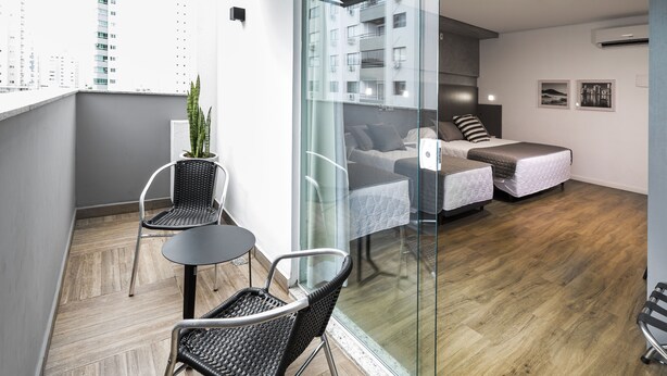 A modern apartment with a balcony, a small dining area, and a bedroom with two beds. - Tropikalya Gold Hotel (Balneário Camboriú)
