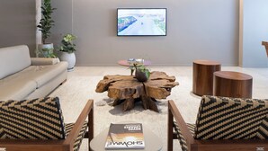 A modern living room with a large TV, a sofa, a coffee table with a plant, and wooden side tables. - Tropikalya Gold Hotel (Balneário Camboriú)
