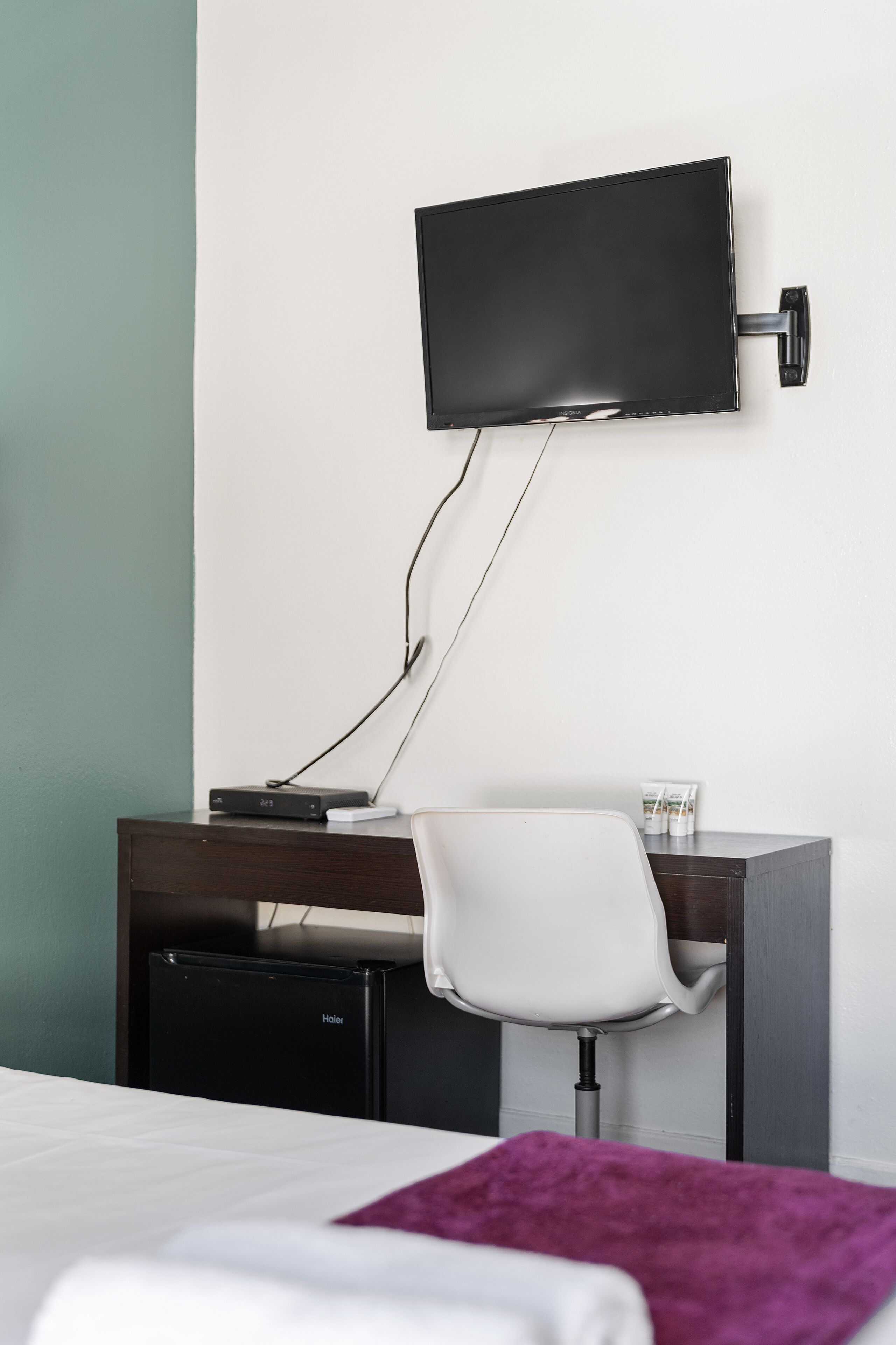 Une chambre d’hôtel comprenant un lit, un bureau avec une chaise, un téléviseur fixé au mur et un petit réfrigérateur.