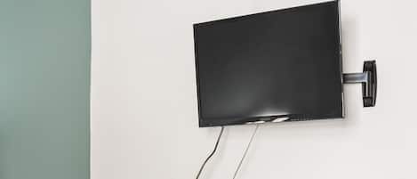 Habitación de hotel con cama, escritorio y silla, televisor montado en la pared y un refrigerador pequeño.