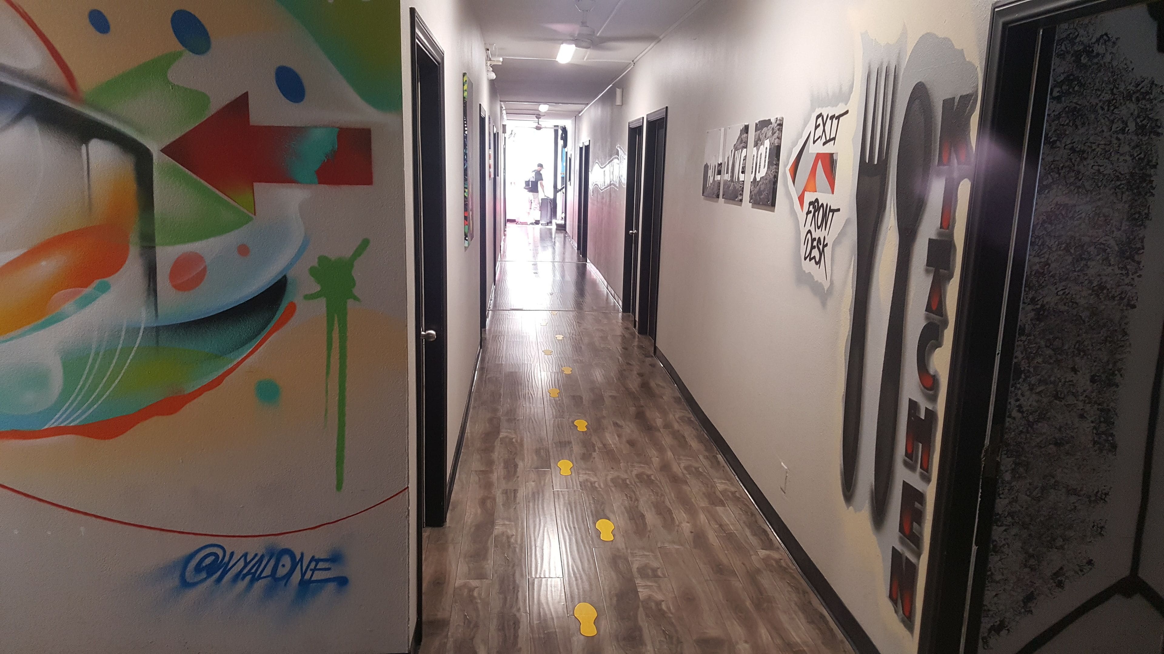 A hallway with colorful graffiti on the walls, a wooden floor, and a ceiling fan.