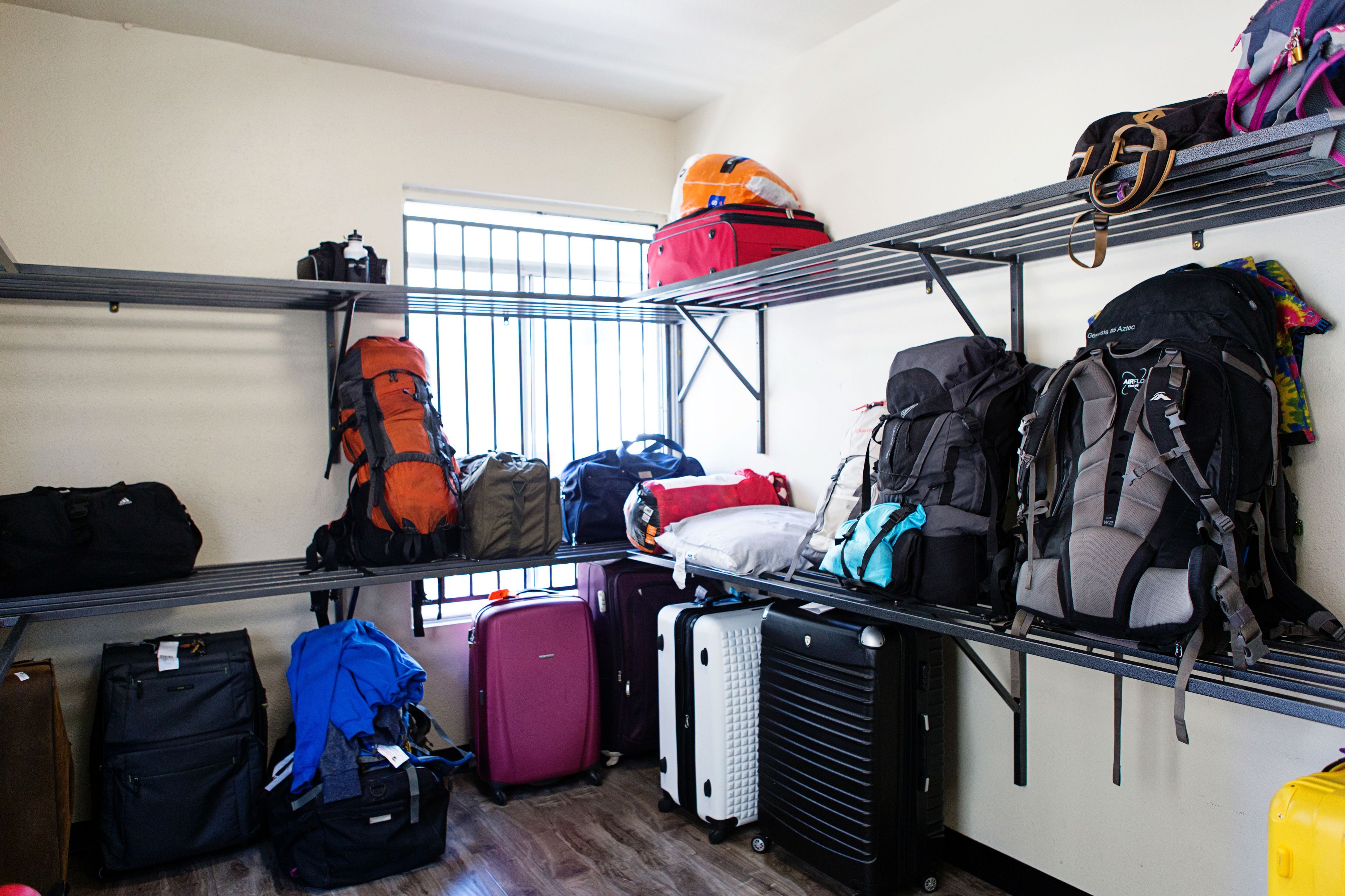 A room with multiple luggage racks filled with suitcases and backpacks, indicating a space designed for travelers.
