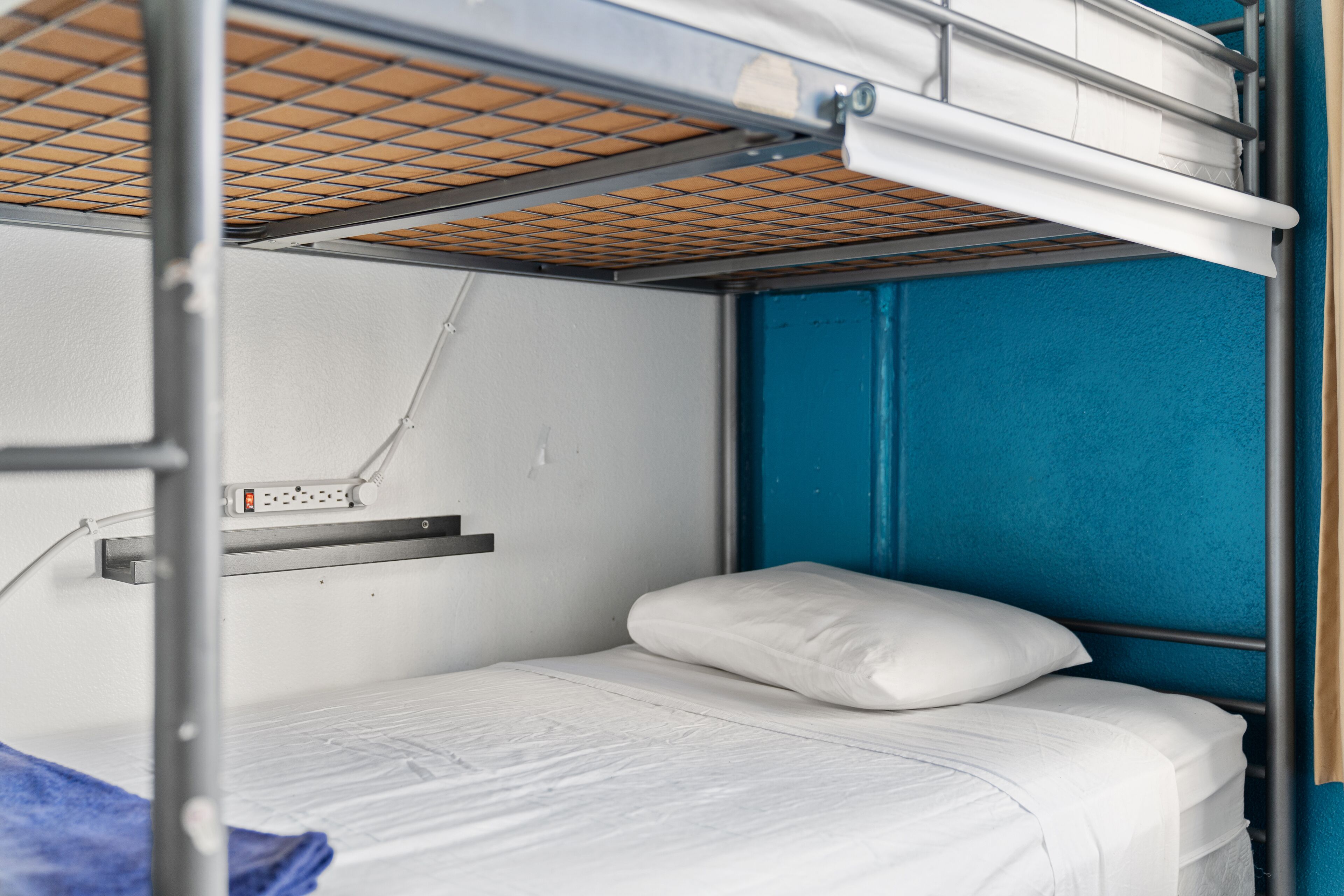 A bunk bed with a mattress and pillows, a power outlet, and a blue wall.