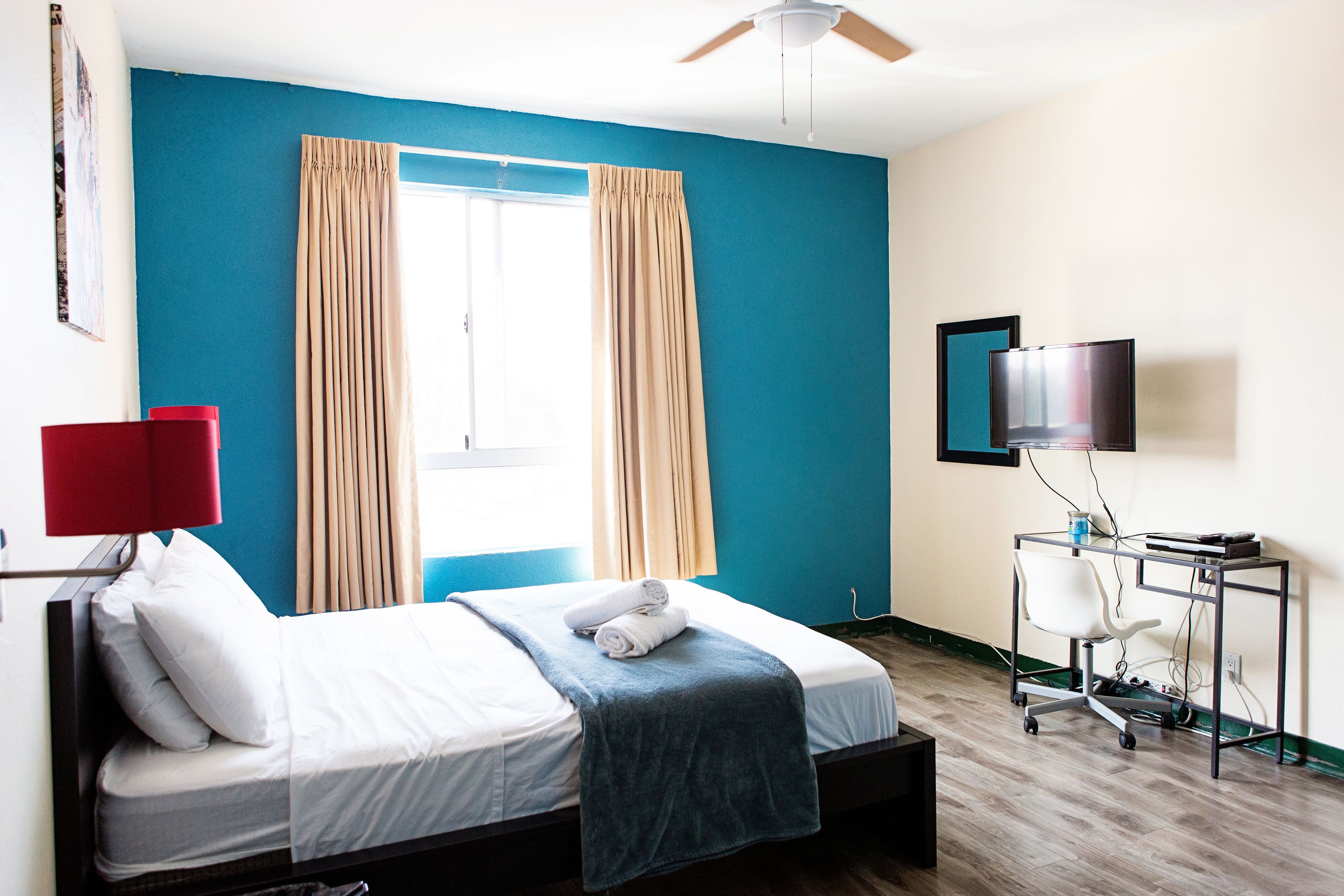 A hotel room with a bed, a desk with a chair, a television, and a window with curtains.