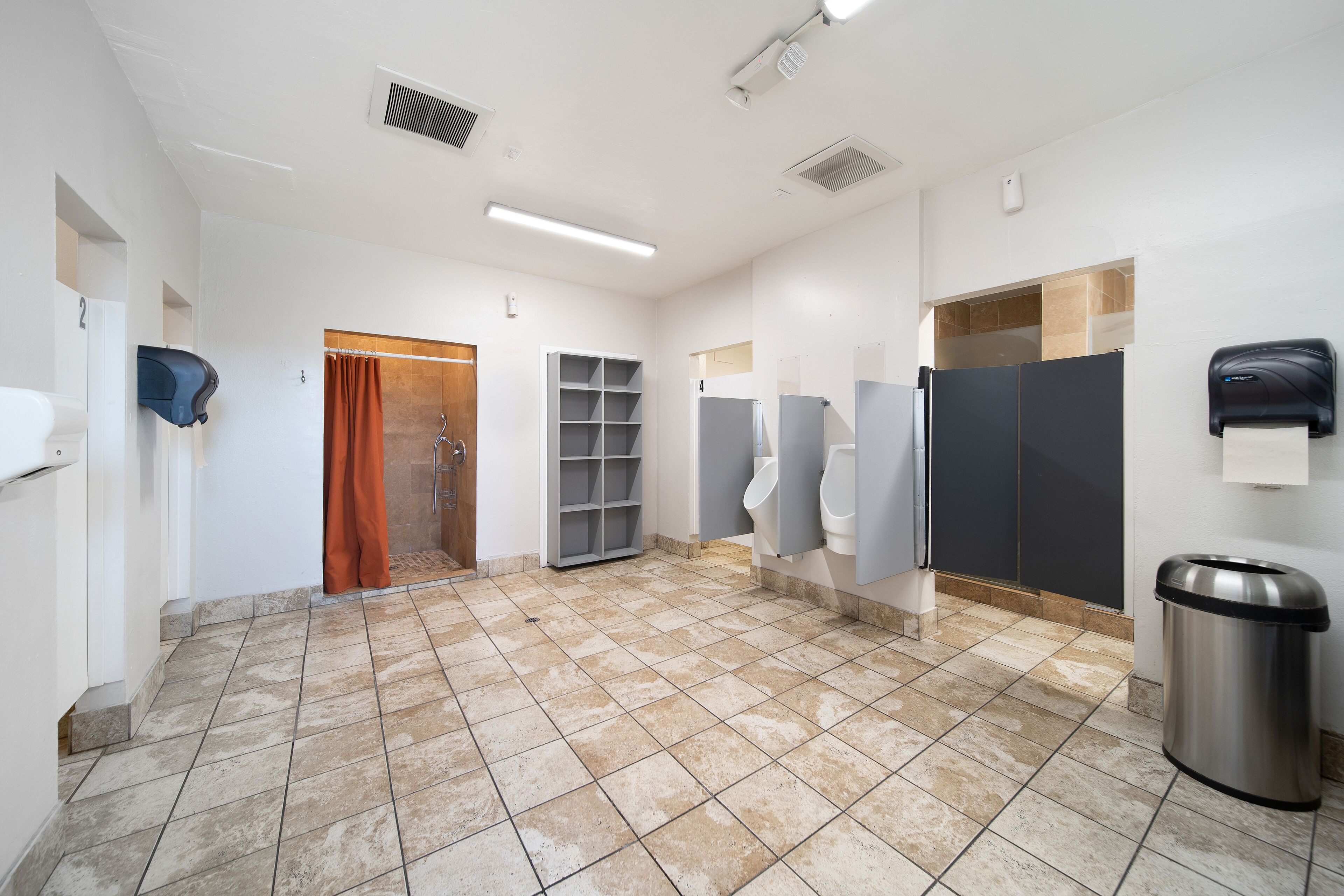 Un bagno pubblico con diversi orinatoi, un cestino e un dispenser di asciugamani.